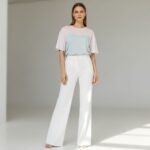 Moderní žena v bílých kalhotách širokých nohavic stojící v osvětleném studiu s neutrálním výrazem