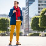 Stylová osoba v městském prostředí s barevným outfitem modrá bunda, žluté kalhoty a červený šátek