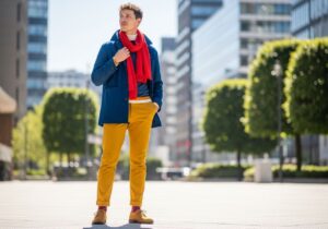 Stylová osoba v městském prostředí s barevným outfitem modrá bunda, žluté kalhoty a červený šátek