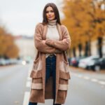 Žena v dlouhém svetru na městské ulici s podzimními barvami v pozadí, přirozené světlo