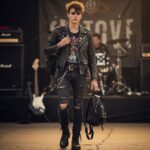 Mladý člověk v kožené bundě a vintage tričku čeká u vstupu na rockový koncert