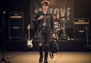 Mladý člověk v kožené bundě a vintage tričku čeká u vstupu na rockový koncert