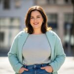 Plus size žena v městském prostředí, oblečená v pohodlném moderním oblečení, usmívající se do kamery
