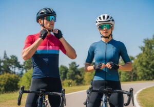 Muži a žena na kolech v cyklistickém oblečení nastavují helmy na slunné cestě v parku.