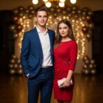 Mladý pár na osmnáctinové oslavě v elegantním oblečení, okolí s balónky a světýlky.