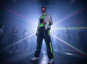 Mladá osoba v techno klubu v neonovém oblečení s brýlemi, teniskami a futuristickými doplňky, světla a dým.
