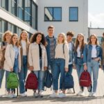 Skupina teenagerů před školou v podzimním oblečení se školními batohy na slunečné ráno